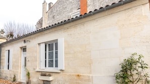 A stone building with a white door and windows, a bell above the door, and a small plant on the right. - Large atypical charming house entirely renovated. (Jonzac)