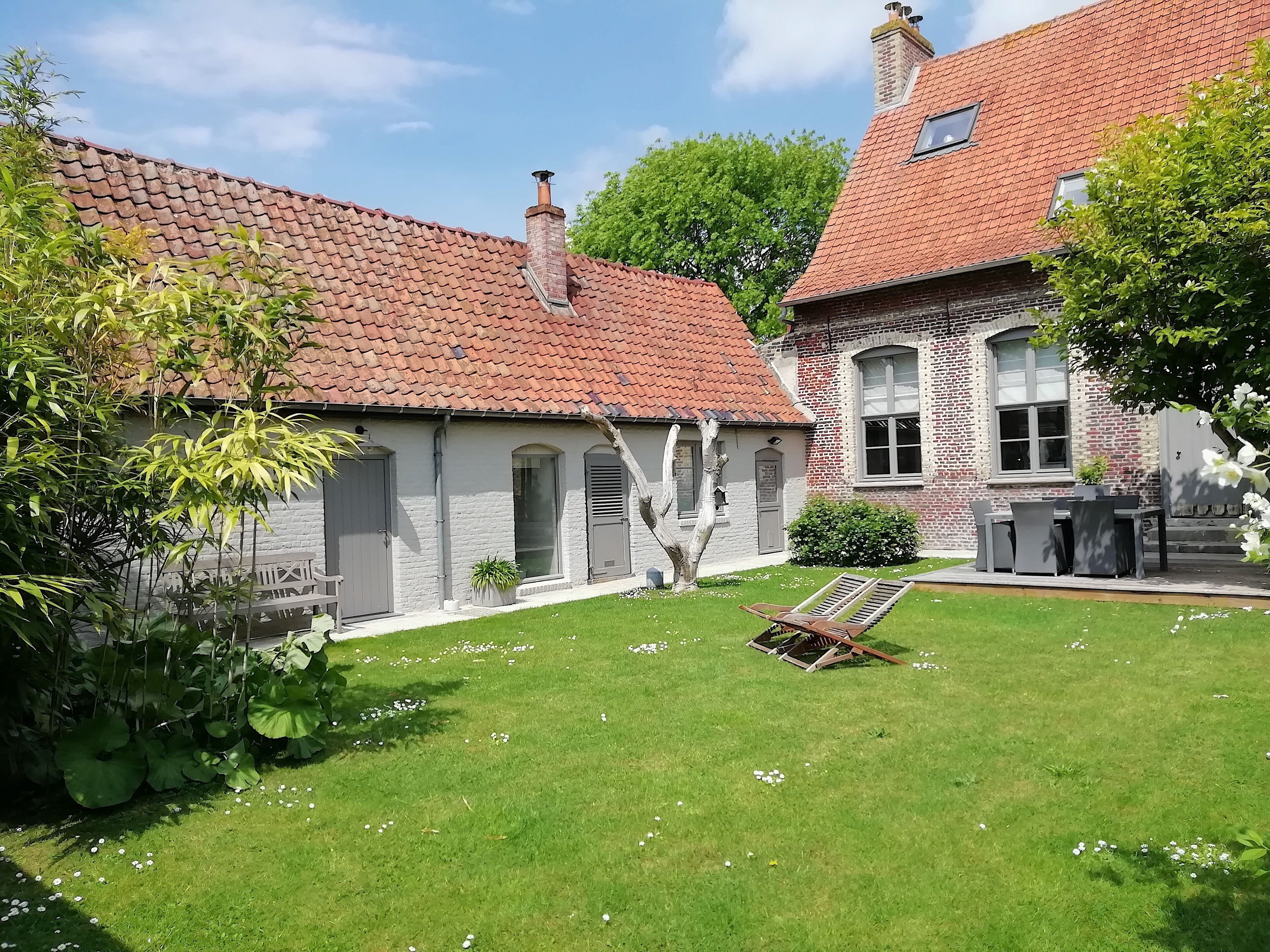 A courtyard with a lawn, a wooden bench, and a brick building with a red-tiled roof.