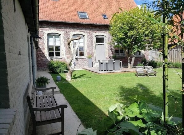 A brick house with a well-maintained lawn, outdoor seating, and a tree.