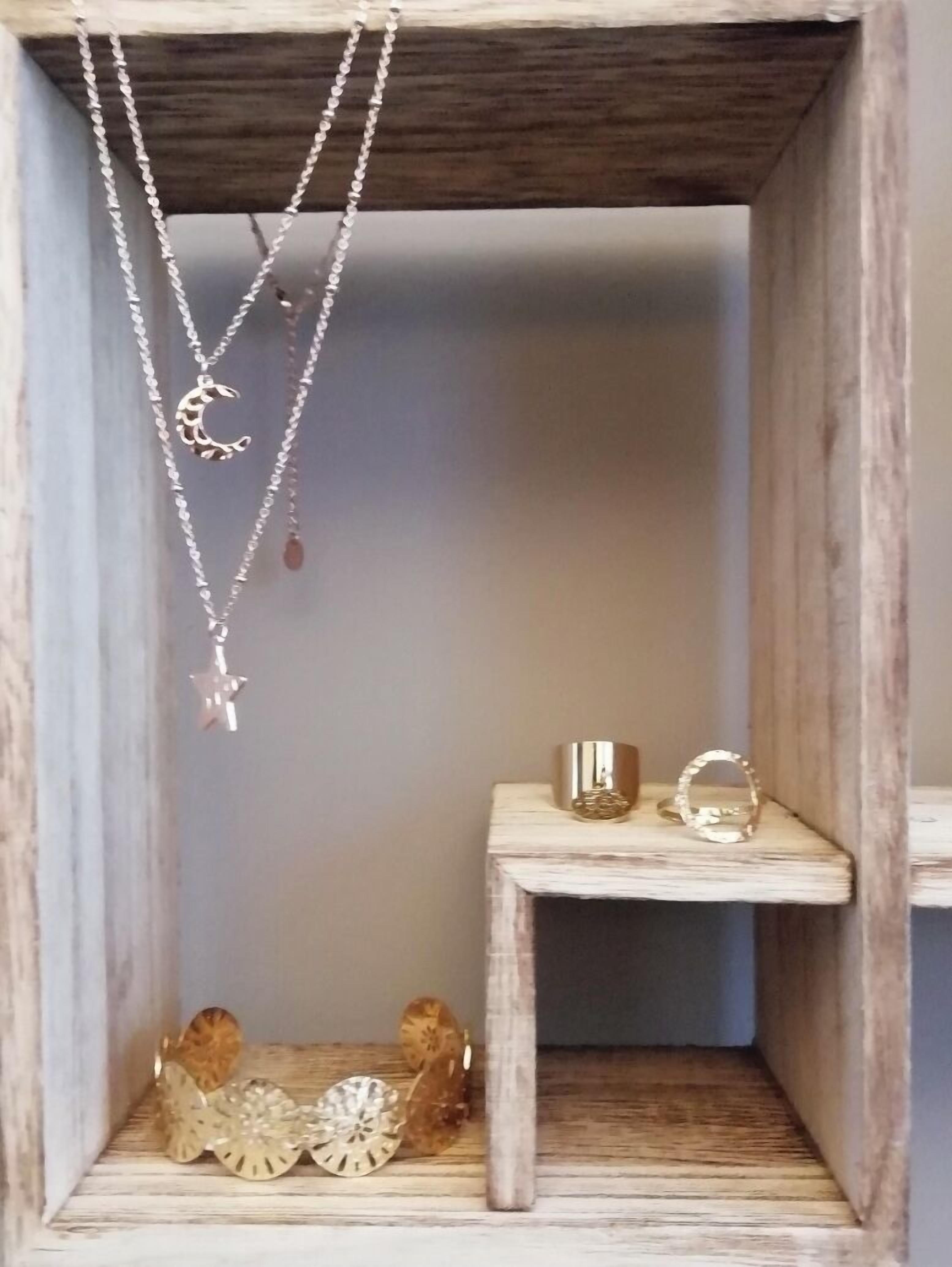 A wooden jewelry box with a shelf containing a crescent moon pendant necklace, a star pendant necklace, and a small golden ring.