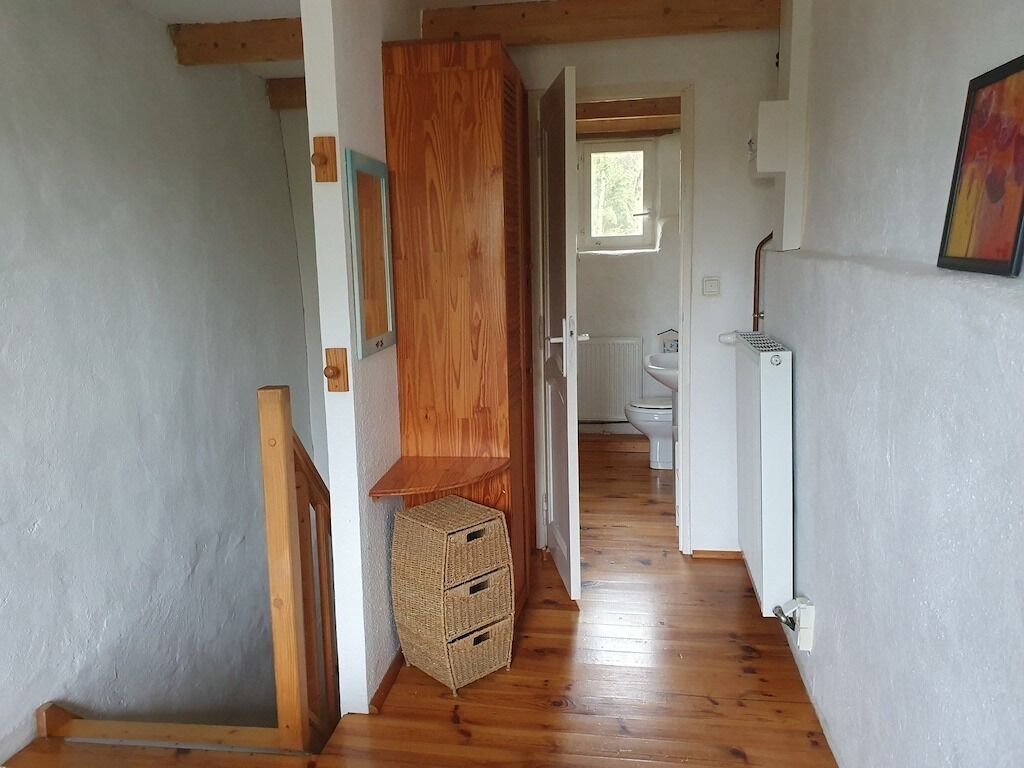 A narrow hallway with wooden flooring and a wooden staircase. A wicker basket is placed near the staircase.