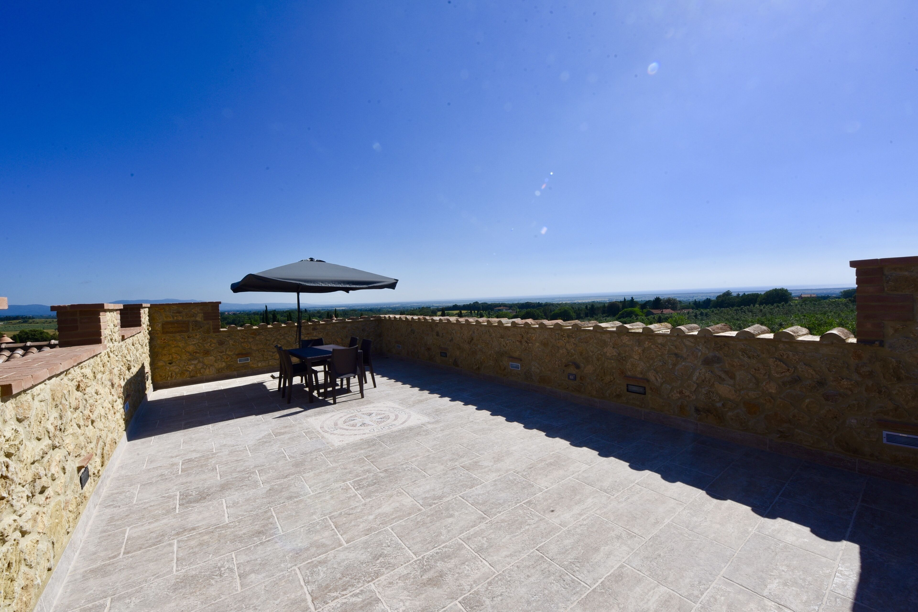 A patio with stone walls, a table, chairs, and an umbrella.