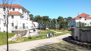 Ein weißes Gebäude mit roten Dächern, einem gepflasterten Weg und einem kleinen Garten mit einem Pavillon.