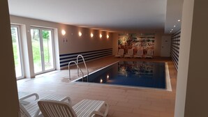 Ein Poolbereich mit gefliestem Boden, einem Pool und weißen Liegestühlen.