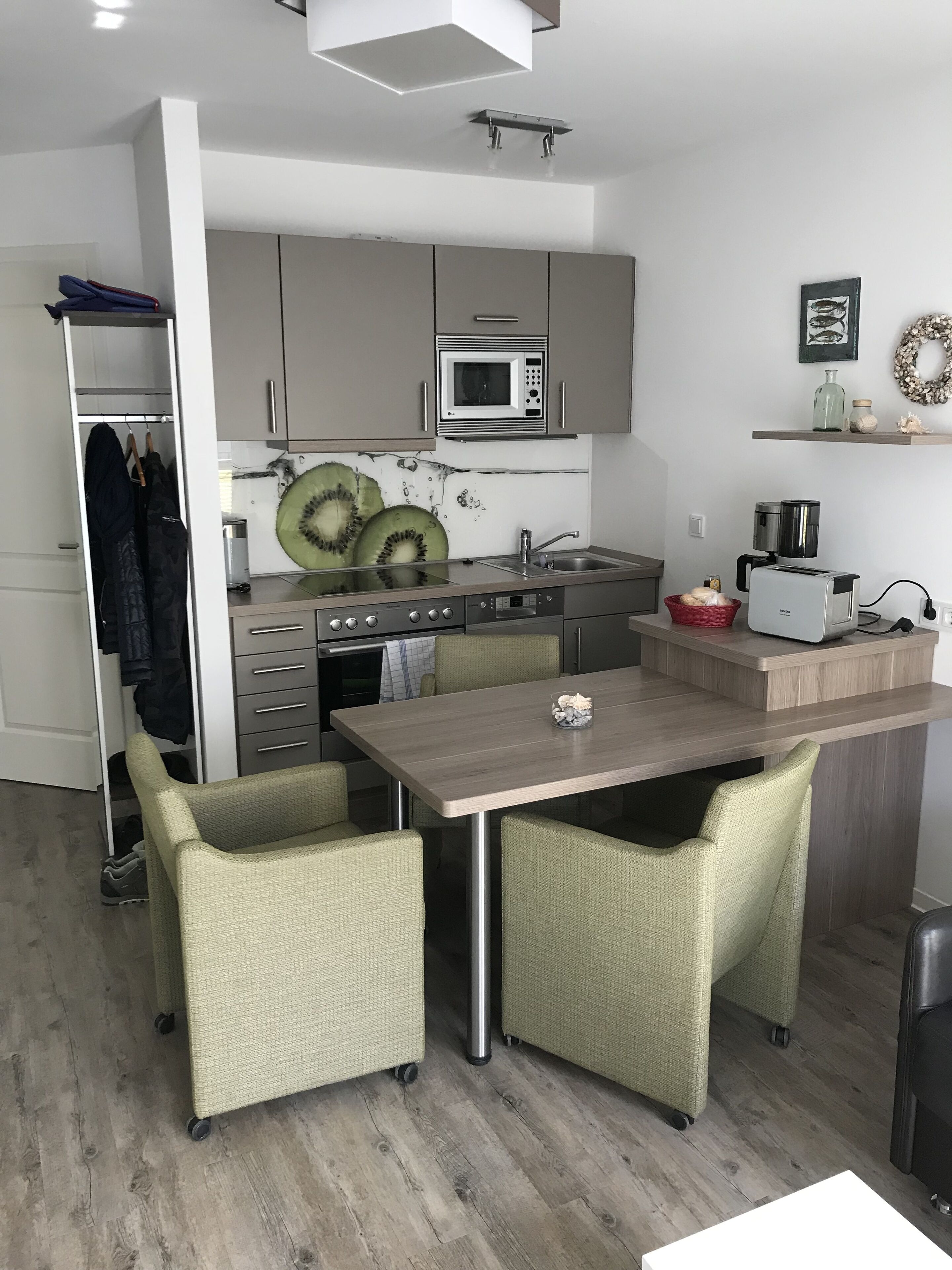 Kompakti keittiö, jossa on mikroaaltouuni, leivänpaahdin ja pesuallas. Keittiössä on ruokapöytä tuoleineen sekä pieni kori pöydällä.