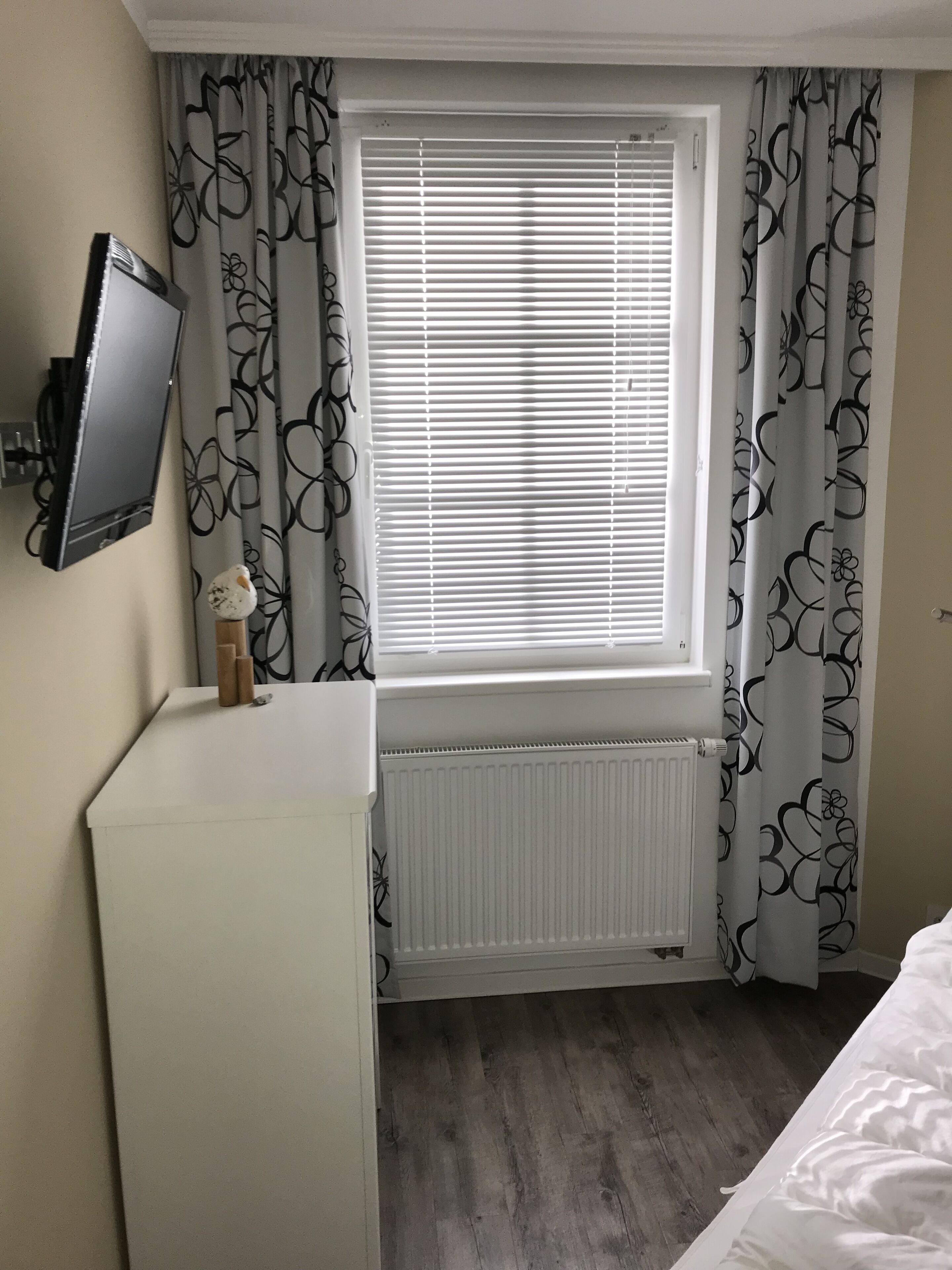 Ein Schlafzimmer mit Fenster, Heizkörper, Wand-Fernseher und Bett.