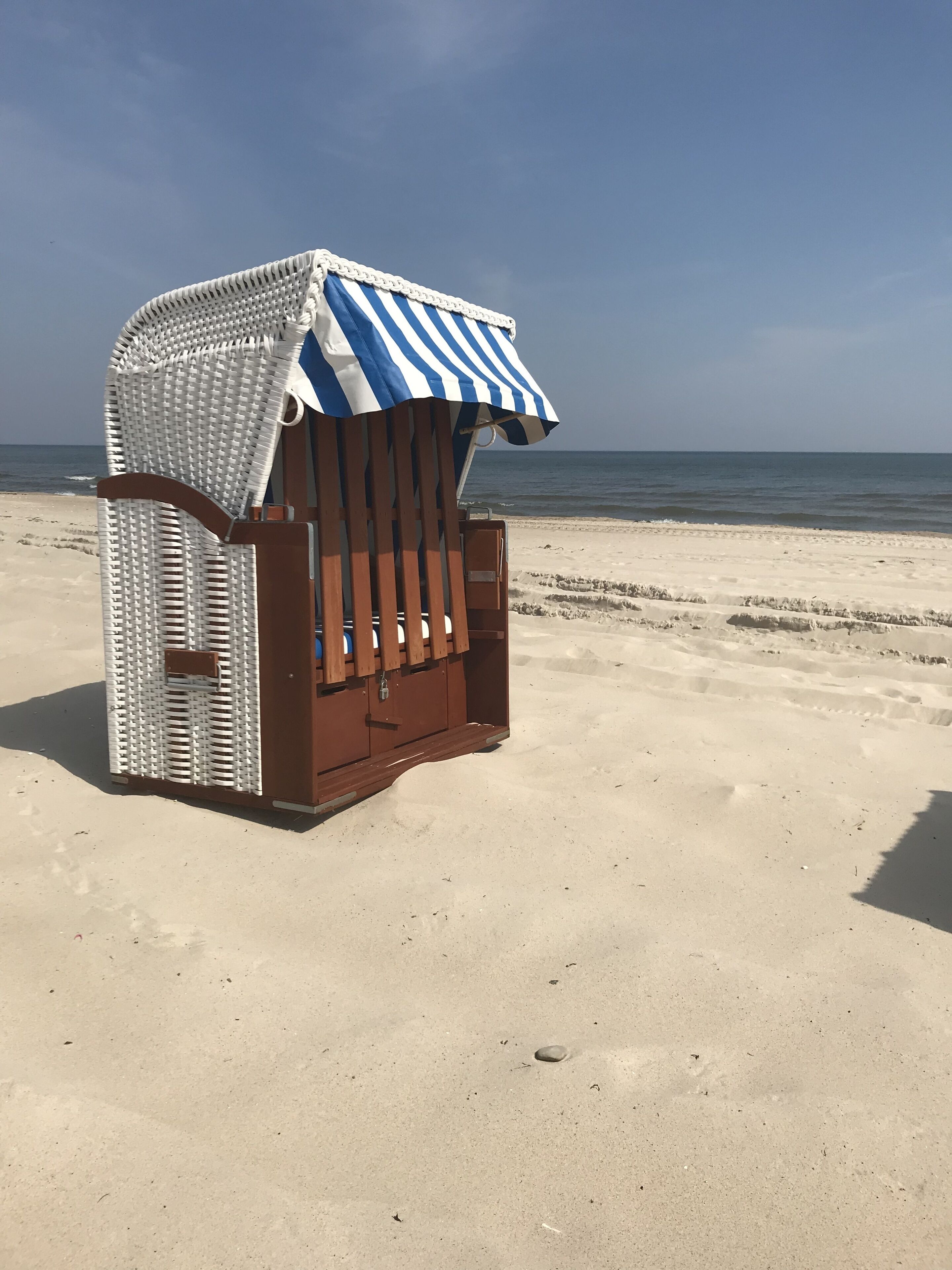 Una estructura de madera junto a la playa con un toldo a rayas, probablemente un quiosco o cabaña, ubicada en una playa arenosa con el océano al fondo.