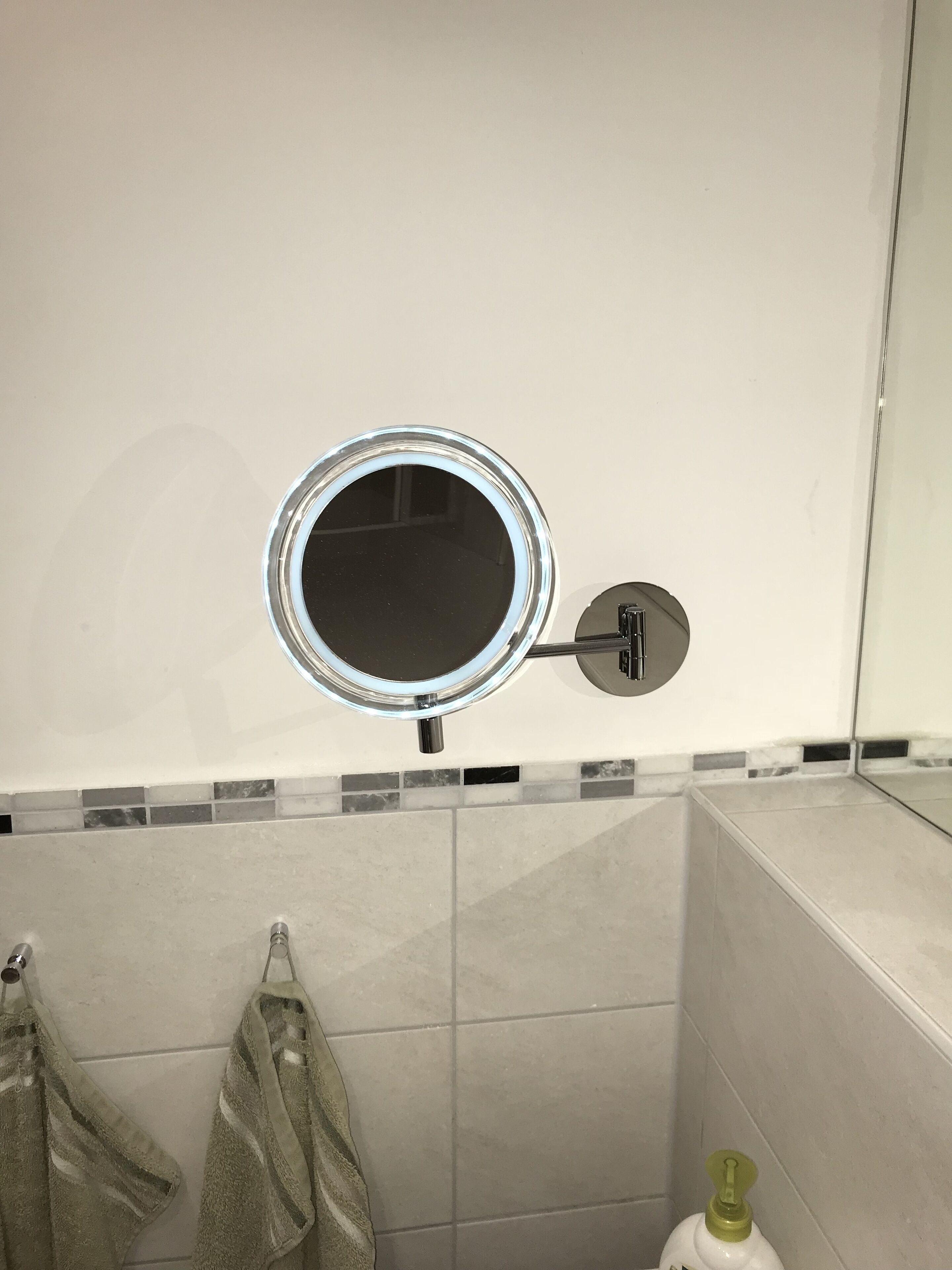 Ein Badezimmer mit einem runden Spiegel an der Wand, einem Handtuchhalter mit Handtüchern und einer Seifenspender.