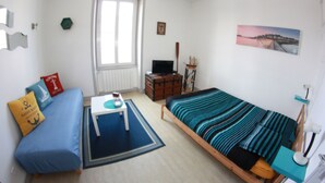 A small, well-lit room with a bed, a sofa, a TV, and a window. - Central apartment near train station  (Saint-Malo)