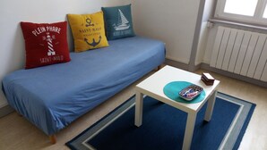 A room with a blue sofa bed, three decorative pillows, a small white table with a tray, and a blue rug. - Central apartment near train station  (Saint-Malo)
