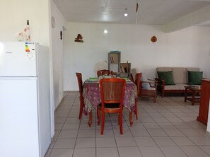 A dining area with a table set for four, surrounded by wooden chairs, a sofa, and a bookshelf. - Villa Le Gommier - Rental in Le Moule, Guadeloupe (LE MOULE)