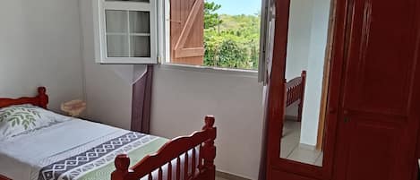 A bedroom with a bed, a wardrobe, a window with a view, and an air conditioning unit.