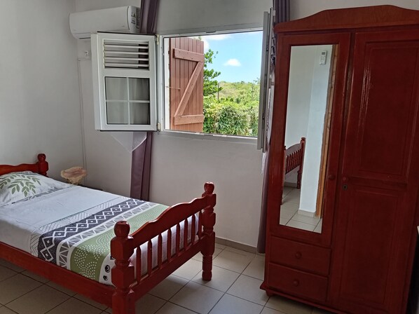 A bedroom with a bed, a wardrobe, a window with a view, and an air conditioning unit.
