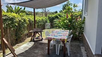An outdoor patio with a table and chairs, a barbecue grill, and a shaded area.