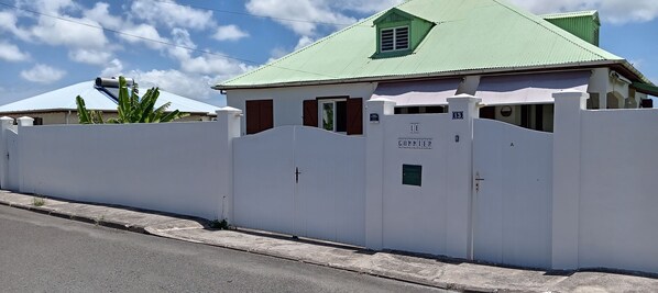 A white building with a green roof, a gated entrance, and a sign reading 'LE GOMMIE'. - Villa Le Gommier - Rental in Le Moule, Guadeloupe (LE MOULE)