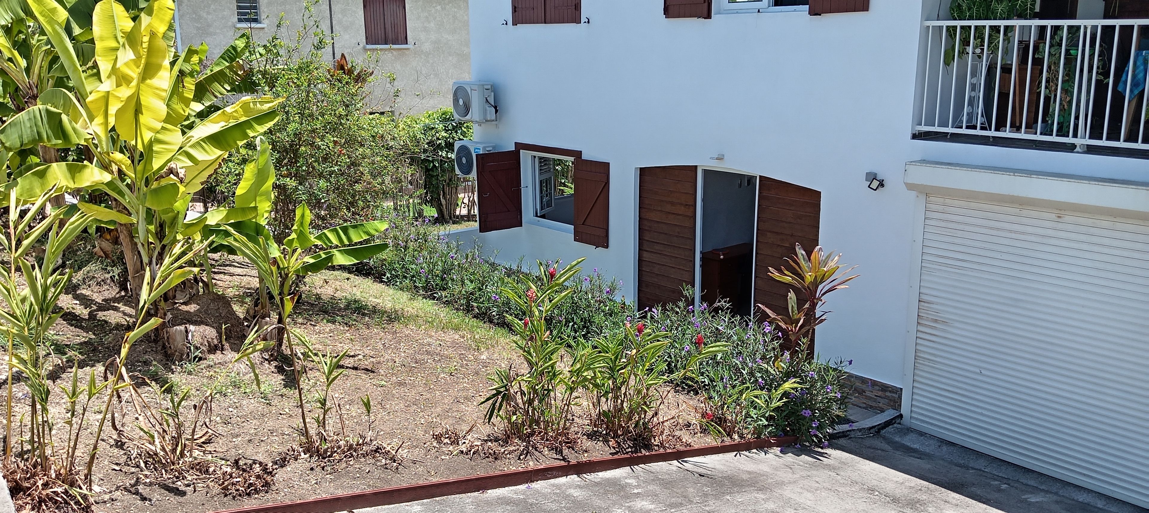 A residential building with a garage, a small garden with various plants, and a balcony with a railing.
