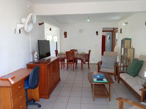 Ein Wohnzimmer mit Fernseher, Holzmöbeln, einer Essecke und einem Bücherregal.