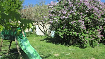 Un toboggan vert dans un espace herbeux, avec des fleurs violettes en pleine floraison et des arbres en arrière-plan.