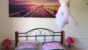 A bedroom with a bed, two bedside lamps, a canopy bed, and a large painting of a pier at sunset. - 2 - Exotic Bungalow T2 & Large Garden near beach  (LA TRINITE)
