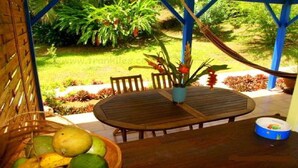 A wooden table with chairs under a blue roof, surrounded by lush greenery and a garden. - 2 - Exotic Bungalow T2 & Large Garden near beach  (LA TRINITE)