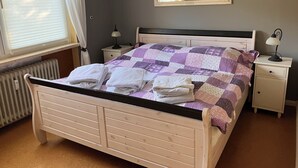 A bedroom with a bed, two bedside tables, a nightstand, a radiator, a window with curtains, and a mirror on the wall. - Quiet vacation oasis with a beautiful view over Bad Lauterberg (Bad Lauterberg)