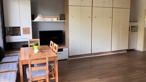 A modern living room with a wooden dining table, chairs, a flat-screen TV, and a large wardrobe. - Quiet vacation oasis with a beautiful view over Bad Lauterberg (Bad Lauterberg)