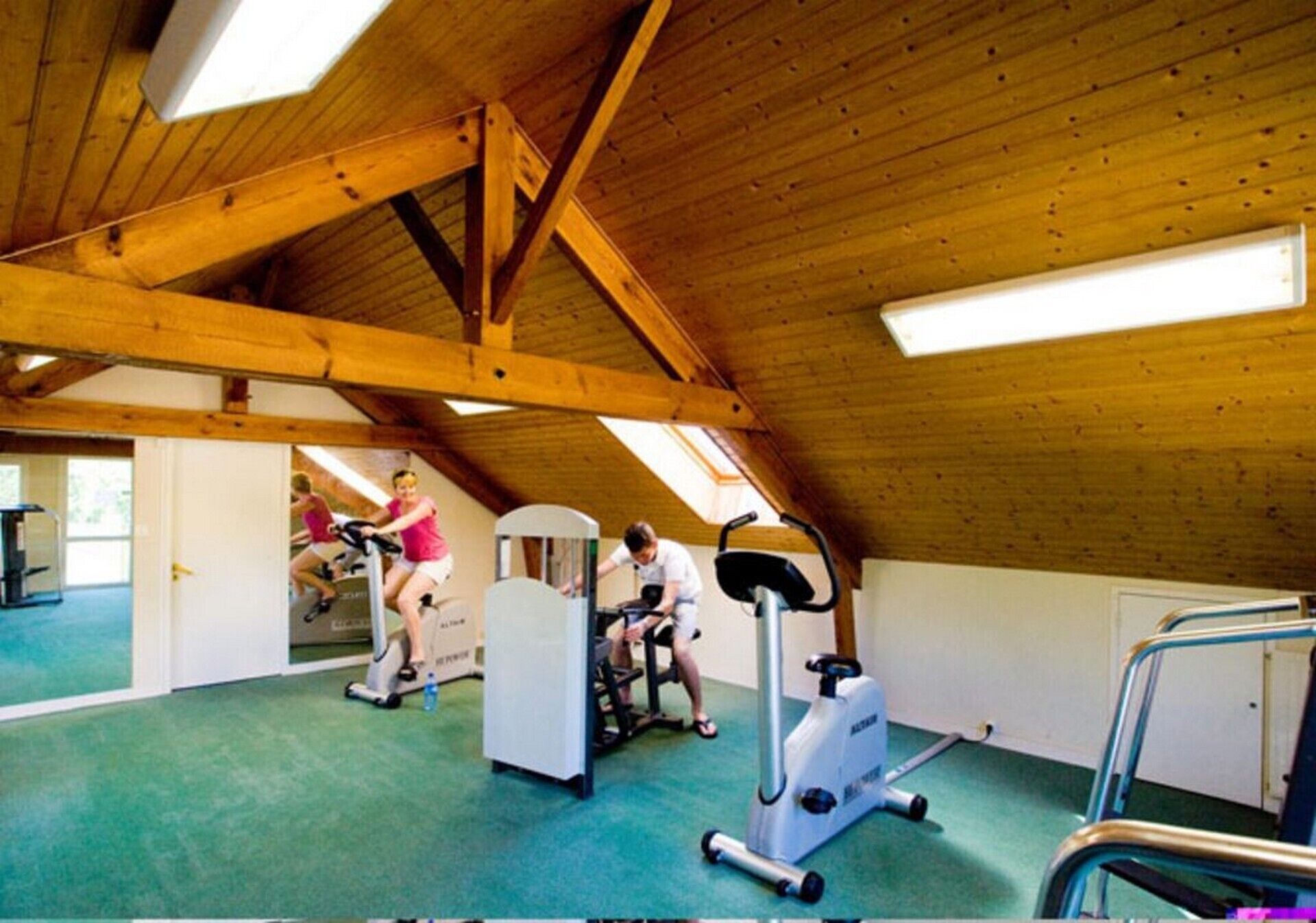 An indoor gym with wooden beams, exercise equipment, and a green floor.