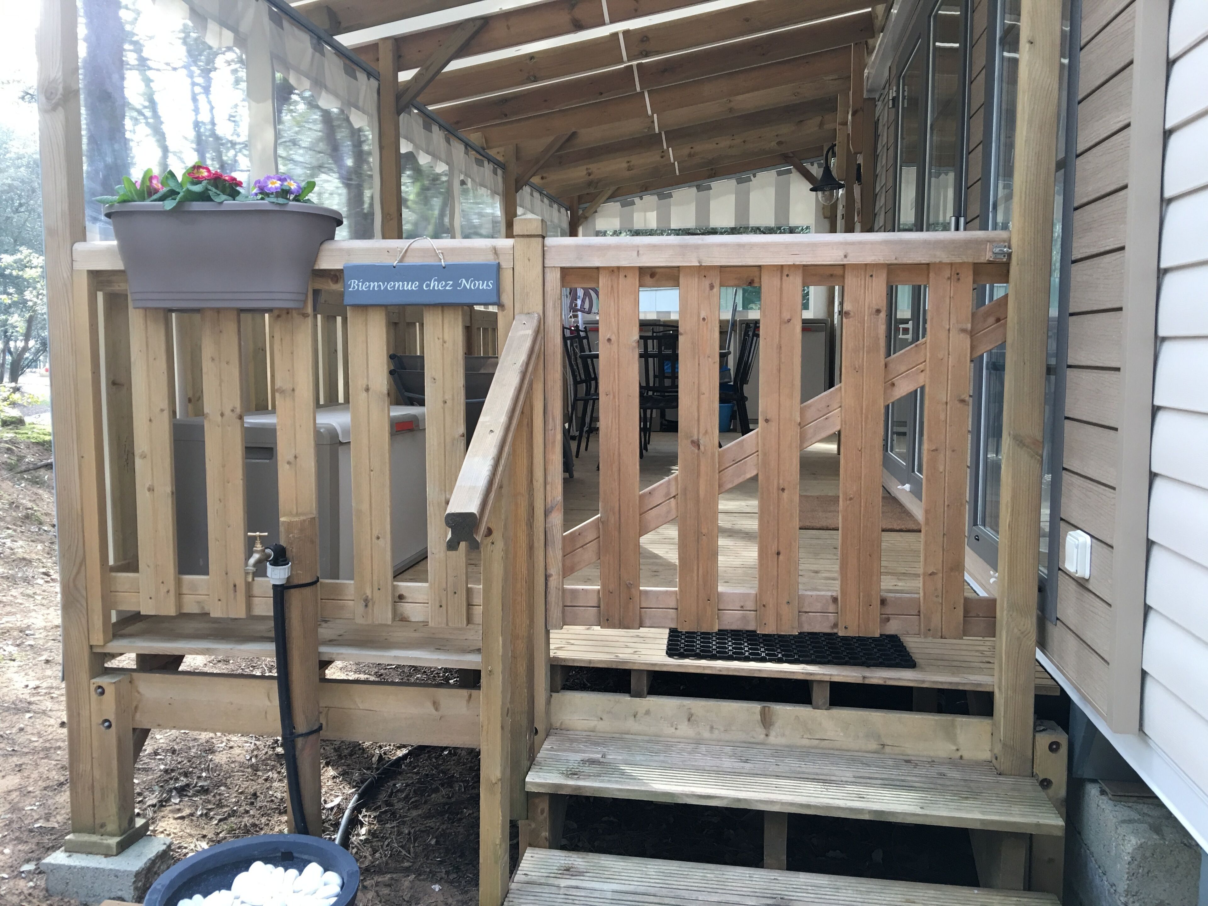 A wooden deck with a sign reading 'Bienvenue chez Nous' and a potted plant with flowers.