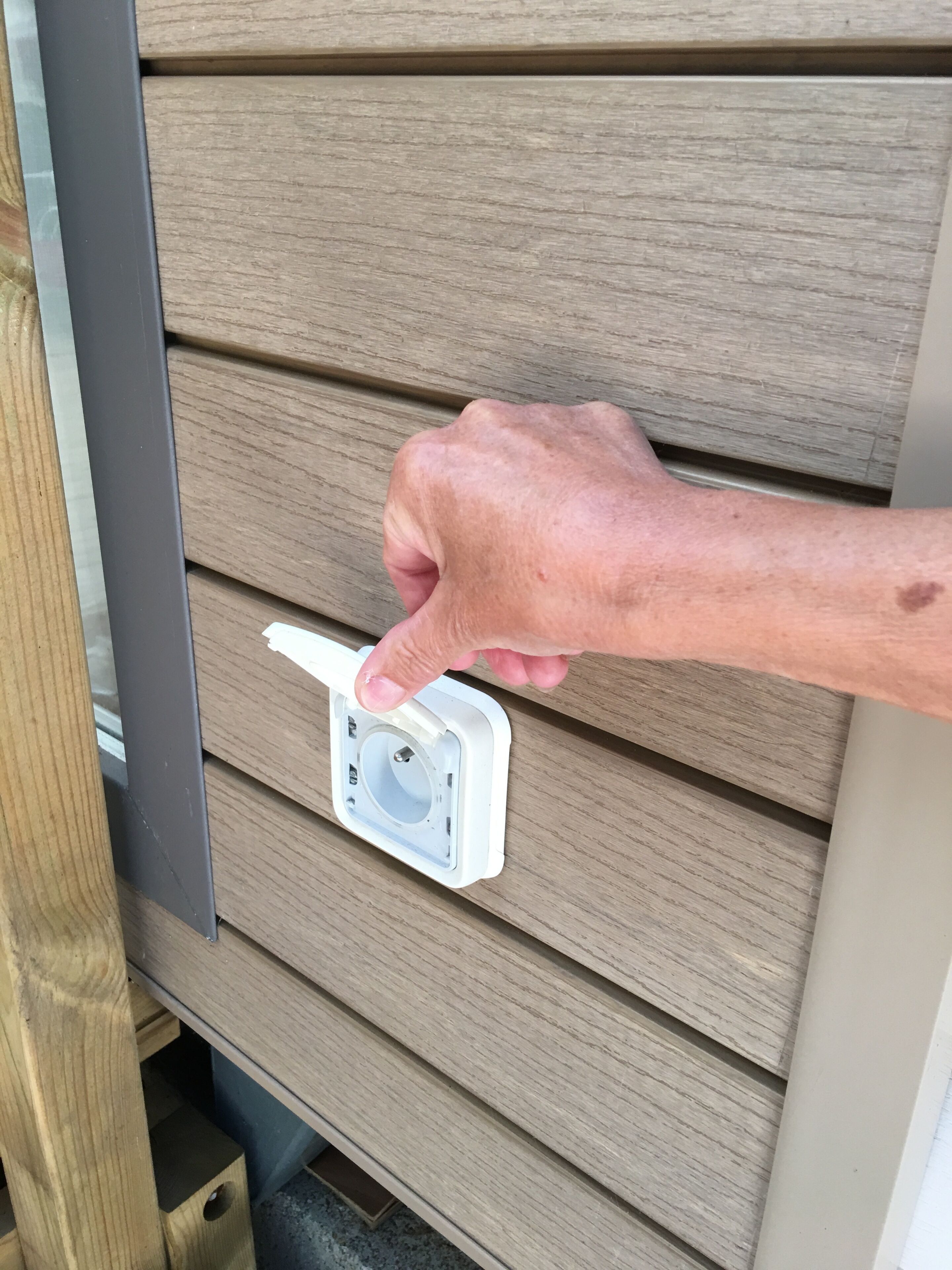 A hand interacting with a white electrical box on a wooden wall.