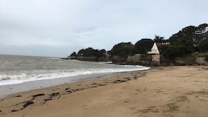 A sandy beach with waves, a rocky cliff, and a building with a pointed roof. - Mobilhome family 6/7 Persons (Saint-Brevin-Les-Pins)