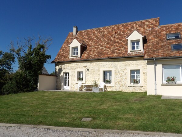 A stone house with a tiled roof, a front porch with a table and chairs, and a well-maintained lawn.