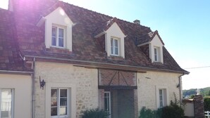 Una casa de dos pisos con fachada de piedra, techo de tejas y un pequeño porche delantero.
