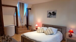 Un dormitorio con cama, lámparas de noche, un cuadro, un aparador de madera, una mesita con adornos y una escalera.