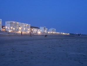 A beachside hotel with multiple floors and balconies, a sandy beach in the foreground, and a clear sky.
