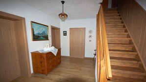 A wooden staircase leading to a second floor, a wooden dresser with drawers, a painting of a mountain landscape, and a door with a small picture above it.