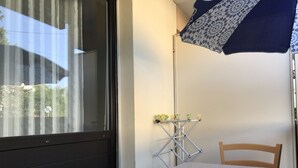 A room with a table, a chair, a window with curtains, a drying rack, and a patterned umbrella. - beautiful T1 30 m2, gated, near downtown, private parking. Wireless (Thonon-Les-Bains)