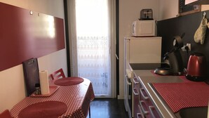 A compact kitchen with a microwave, toaster, and kettle. There is a table with a checkered tablecloth and a chair. The kitchen has a small window with lace curtains. - beautiful T1 30 m2, gated, near downtown, private parking. Wireless (Thonon-Les-Bains)