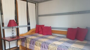 Una camera da letto con un letto, cuscini rossi, una lampada rossa su un comodino e una finestra con tende.