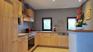 A modern kitchen with wooden cabinets, stainless steel appliances, and a window with a view. - Cottage "Esprit Cozy" 2/4 people (Ostheim)