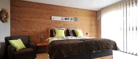 Een moderne slaapkamer met een houten hoofdbord, een groot bed met beddengoed met een patroon, een fauteuil en een nachtkastje met een lamp.