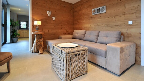 A modern living room with a wooden wall, a sofa, a wicker coffee table, and a lamp. - Cottage "Esprit Cozy" 2/4 people (Ostheim)