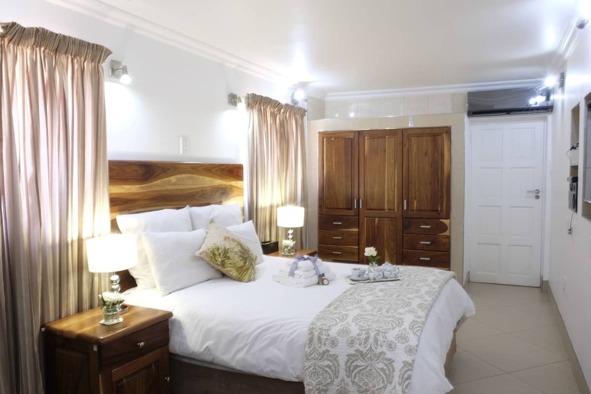 A well-lit bedroom with a large bed, wooden wardrobe, and a white door.