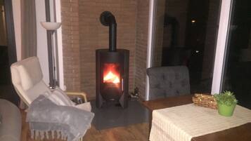 Ein gemütliches Zimmer mit Kamin aus Backsteinen, einem bequemen Sessel, einem Tisch mit einer grünen Pflanze und einer Lampe.