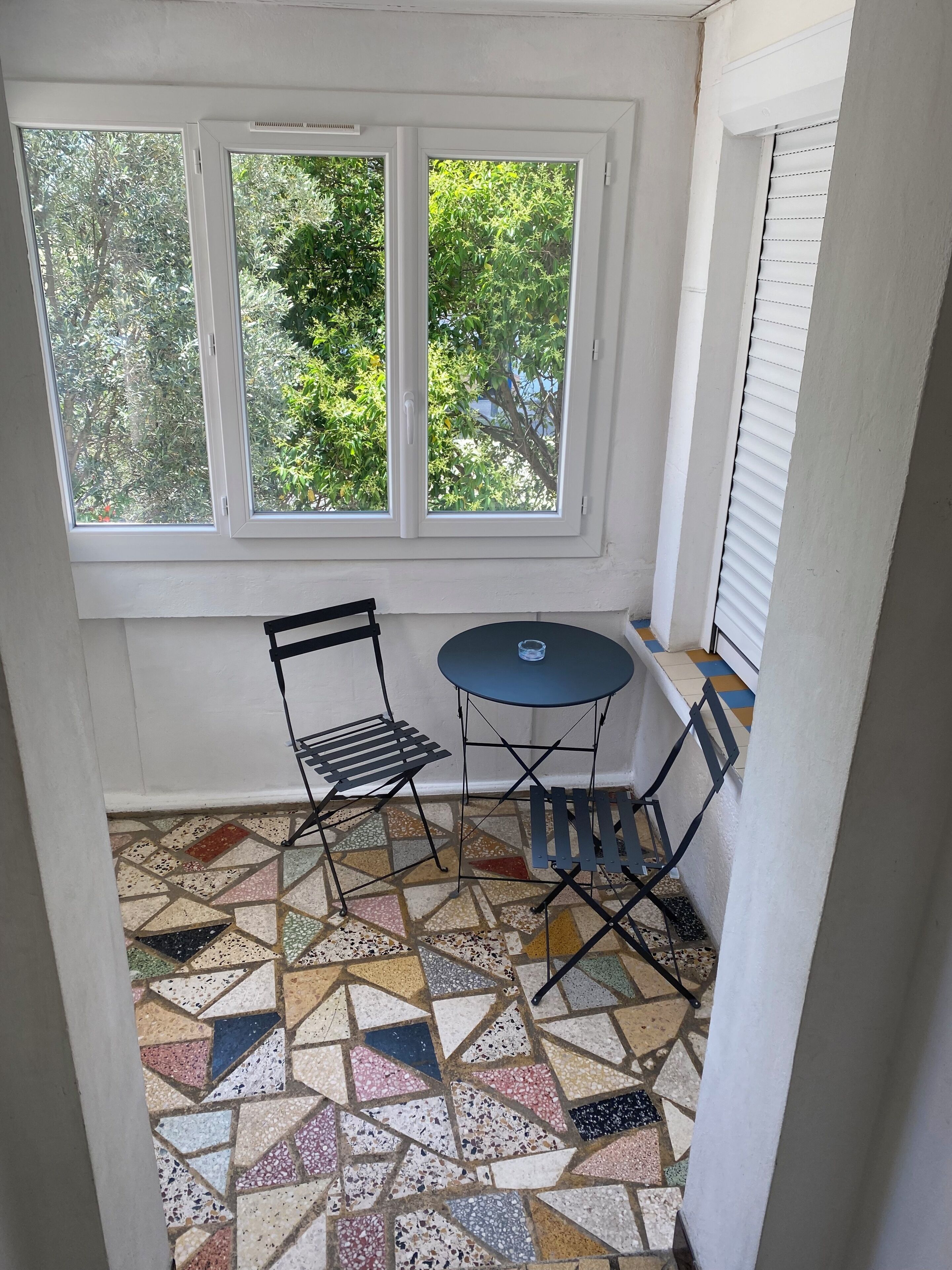 Un petit patio clos avec une fenêtre, une table et une chaise.