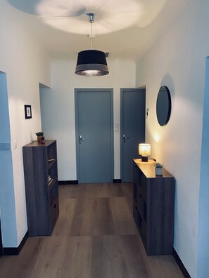 A hallway with a ceiling fan, a door, a wall-mounted mirror, and a small table with a lamp.