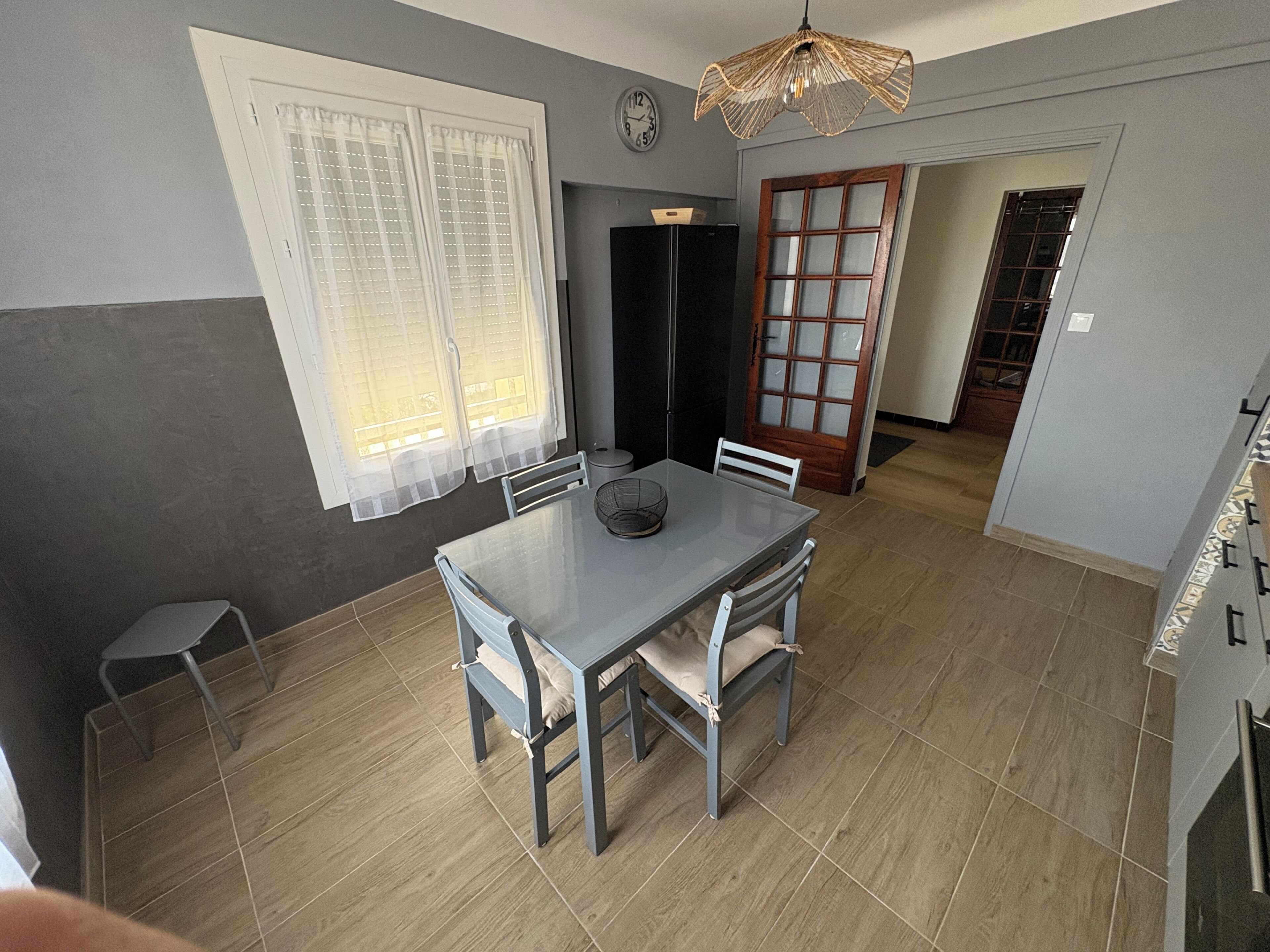 A dining area with a table and chairs, a clock on the wall, and a door leading to another room.