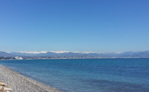 A coastal view with a pebble beach, calm sea, and distant snow-capped mountains. - Nice quiet apartment with pool near beach and city. (Antibes)