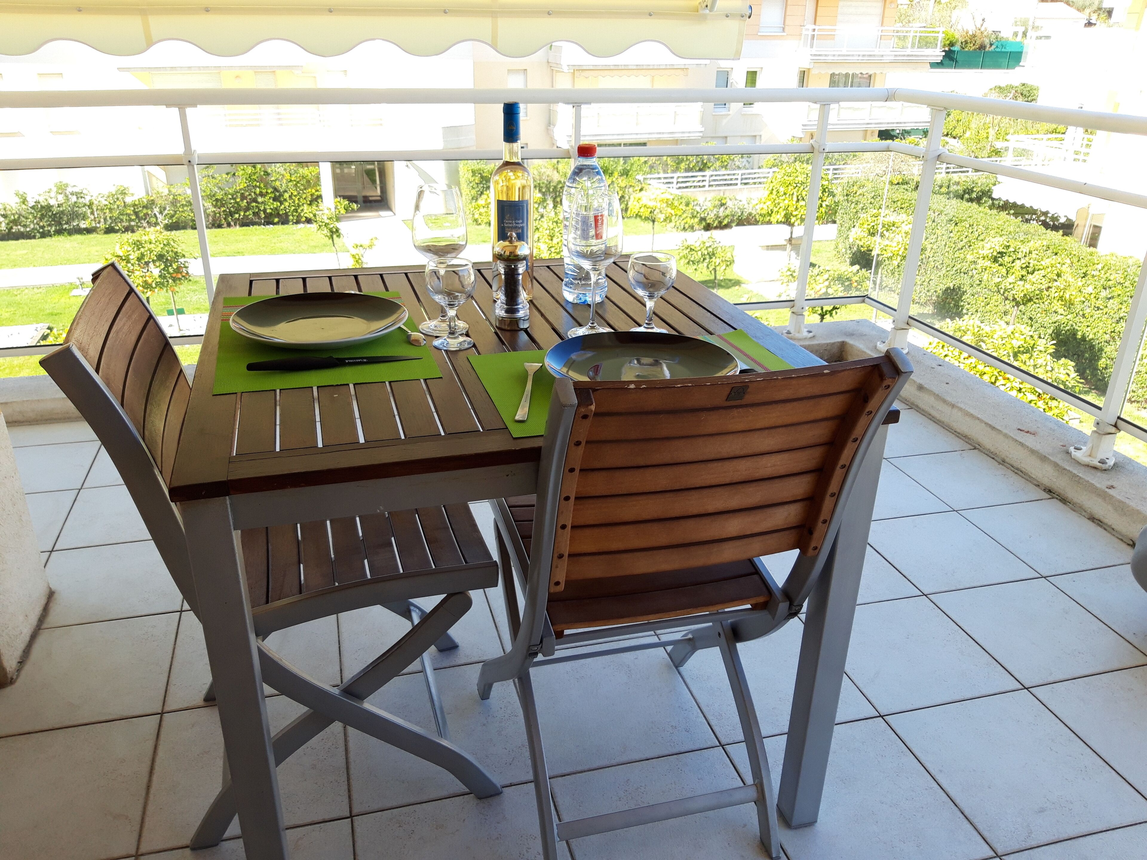 Mesa para dos en un balcón con vista a un jardín y edificios.