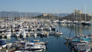 Un port de plaisance où de nombreux bateaux sont amarrés, un grand navire de croisière en arrière-plan et une structure ressemblant à un château à l’horizon.