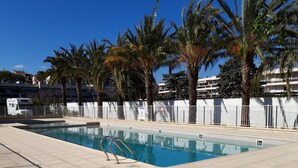 Une piscine avec un escalier en métal, entourée de palmiers et d’une clôture blanche.